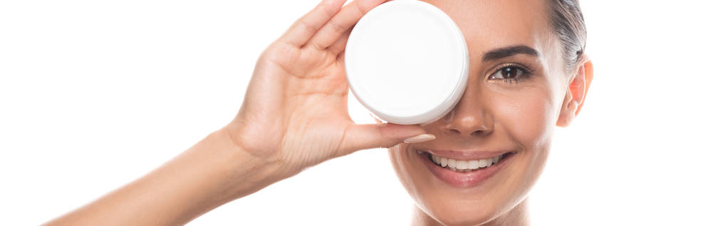 plano panorámico de mujer sonriente sosteniendo contenedor con crema cosmética aislada en blanco
 - Foto, Imagen