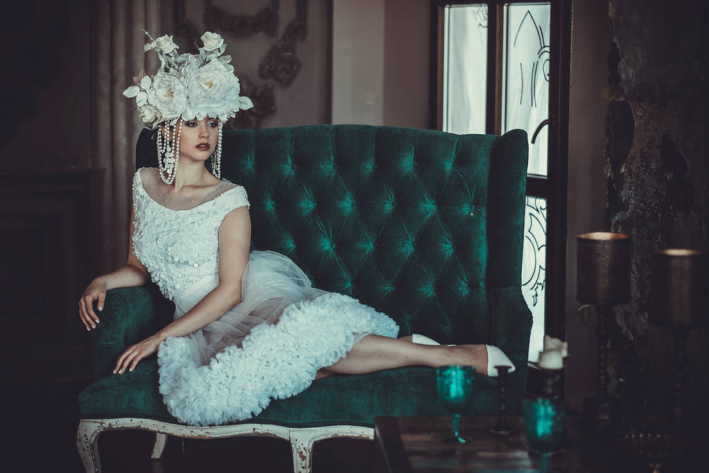 Beyaz elbise giyen güzel genç gelin ve çiçekler çelenk bir sandalyeye oturur. Lüks Saray. - Fotoğraf, Görsel