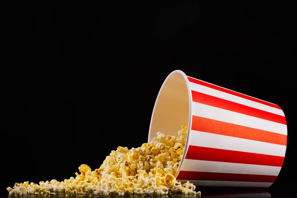 Scattered popcorn from paper striped bucket isolated on black background - Photo, Image