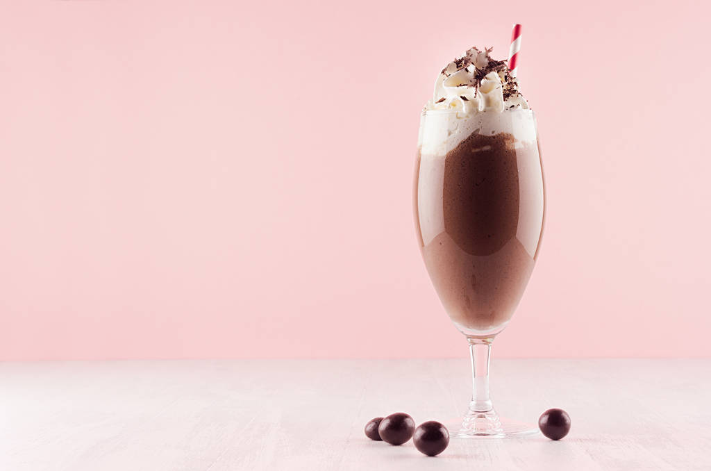 milkshake au chocolat avec crème fouettée sucrée, paille et bonbons dans un intérieur moderne rose élégant sur une table en bois blanc, espace de copie
. - Photo, image