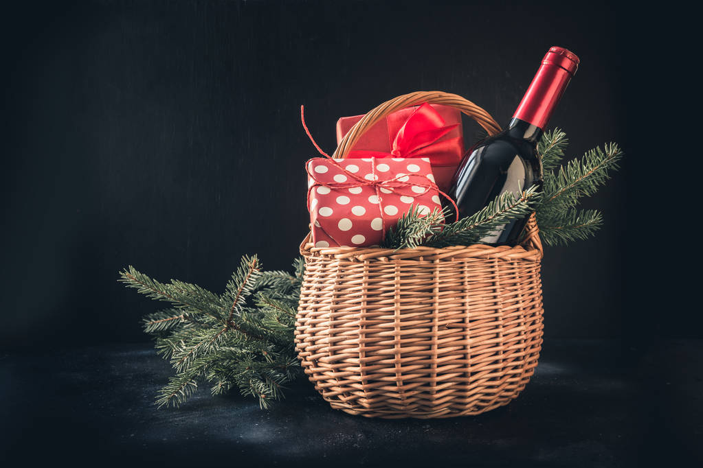 Χριστουγεννιάτικο δώρο καλάθι με κόκκινο κρασί και δώρο στο μαύρο. Χώρος για τους χαιρετισμούς σου. Χριστουγεννιάτικη κάρτα. - Φωτογραφία, εικόνα