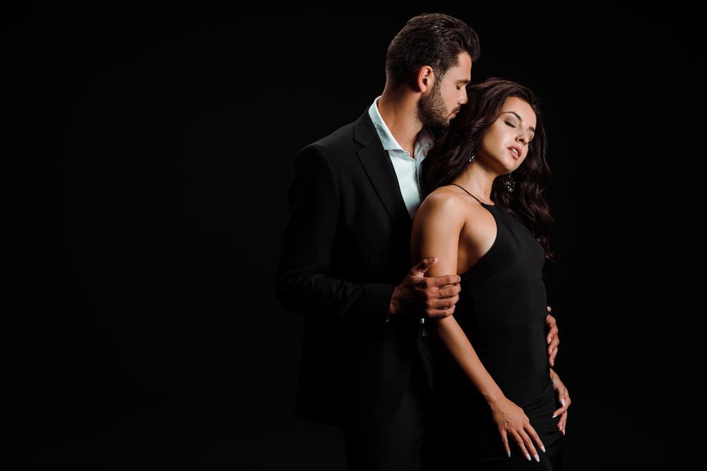 schöner Mann umarmt Frau mit geschlossenen Augen in schwarzem Kleid  - Foto, Bild