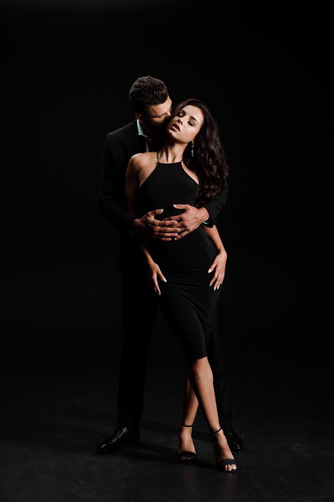Mann umarmt Frau mit geschlossenen Augen im schwarzen Kleid  - Foto, Bild