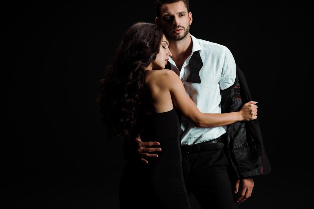 young beautiful woman undressing handsome bearded man isolated on black  - Photo, Image