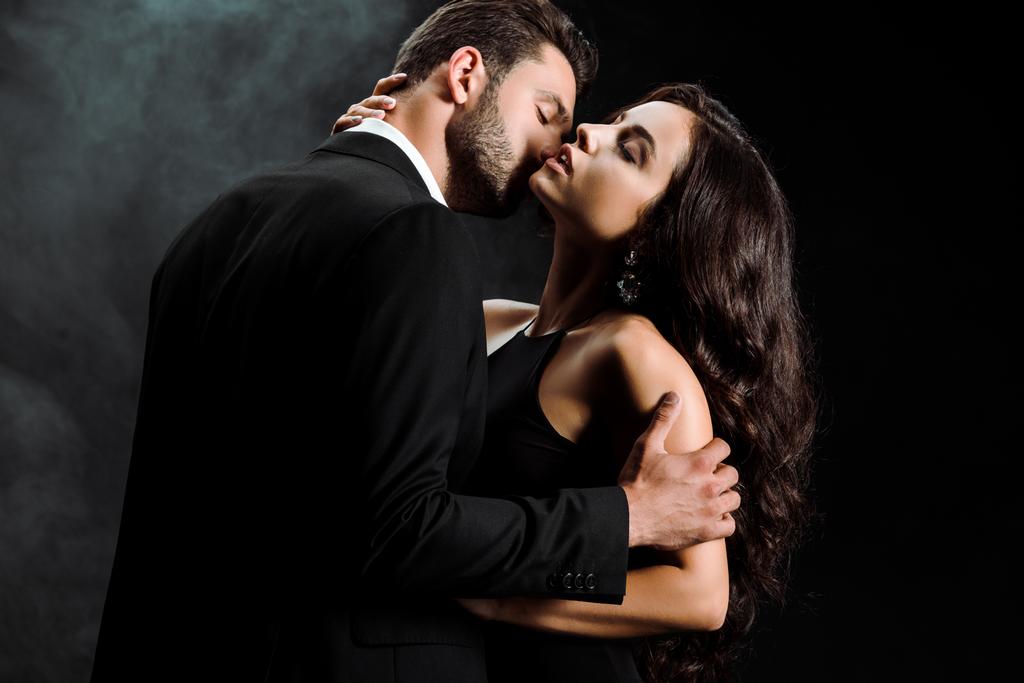 przystojny Brodaty człowiek stojący i przytulanie kobieta z zamkniętych oczach na czarnym z dymem  - Zdjęcie, obraz