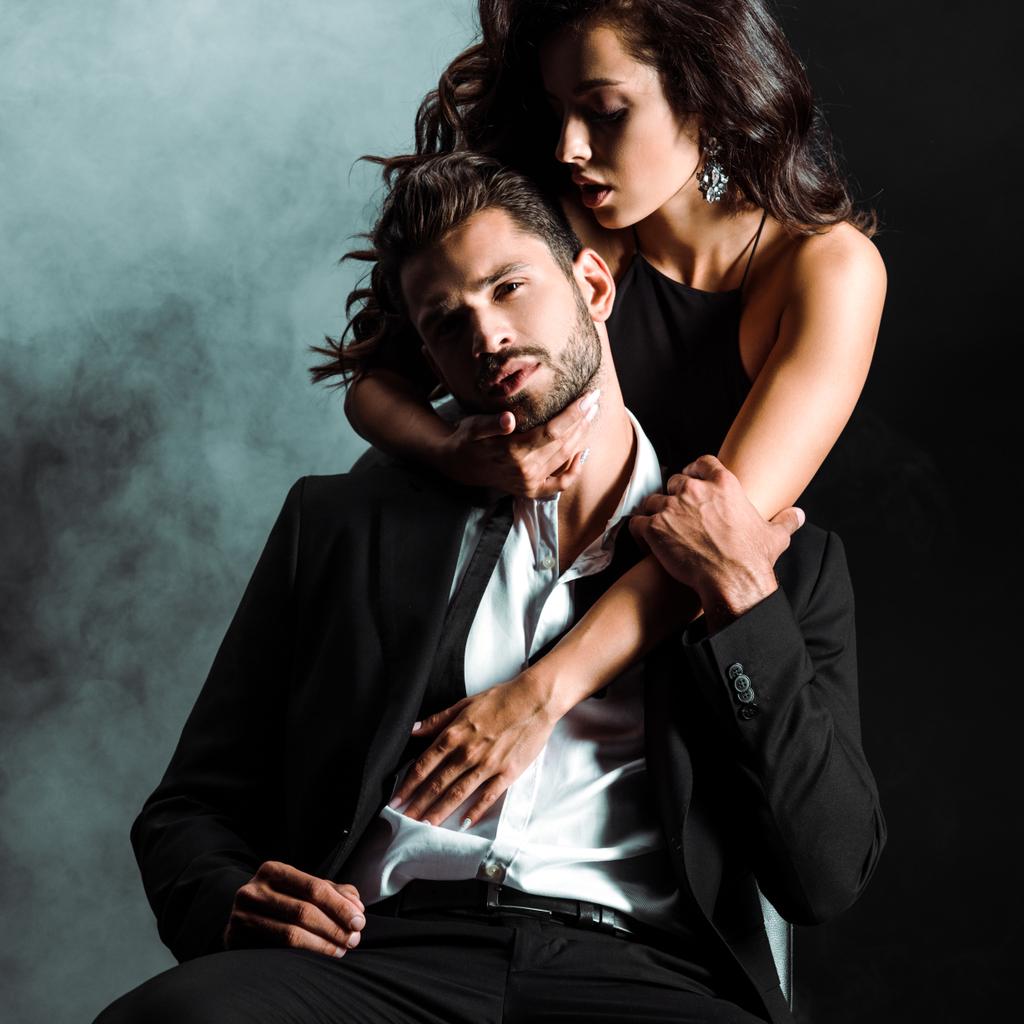 passionate woman standing and hugging handsome bearded man on black with smoke  - Photo, Image