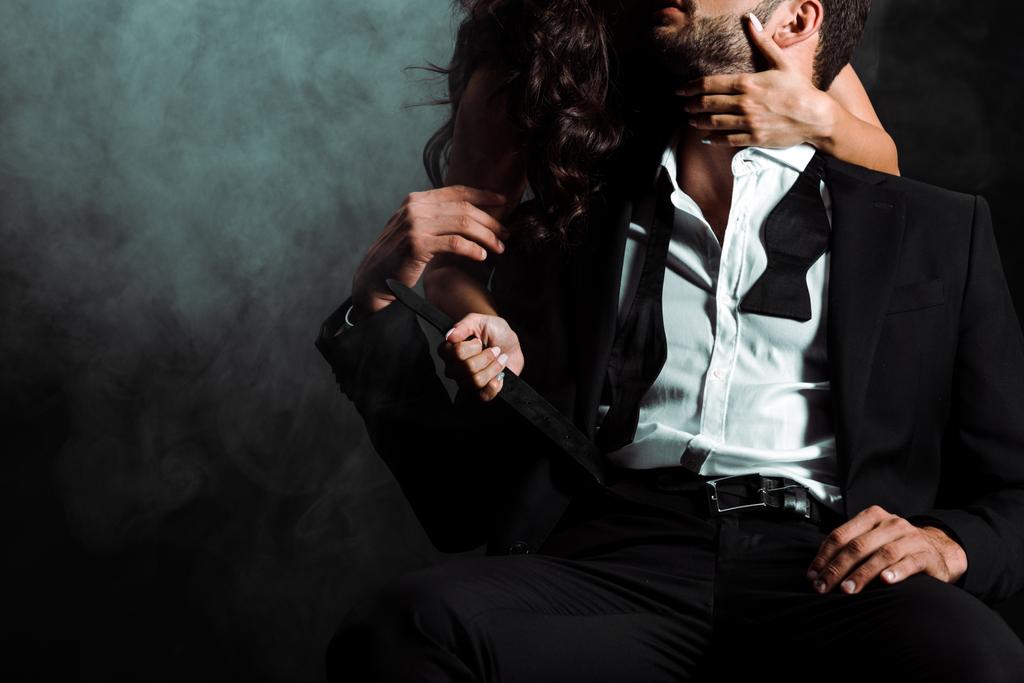 vue recadrée de la femme debout et touchant homme barbu sur noir avec de la fumée
  - Photo, image