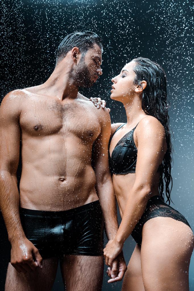 黒の雨滴の下でガールフレンドと一緒に立っている濡ったシャツのない男  - 写真・画像