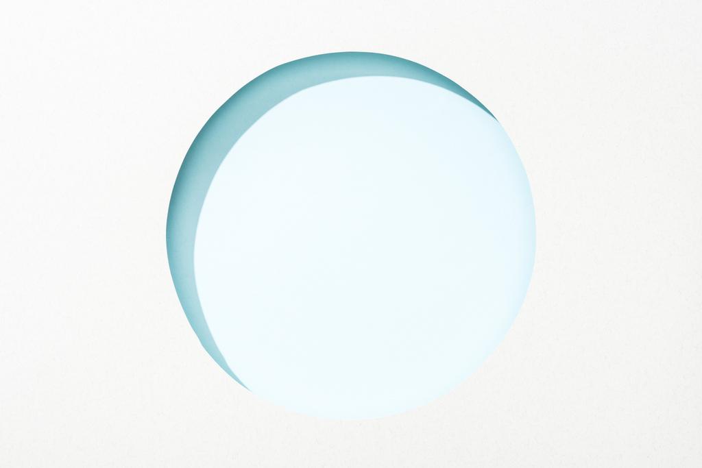 Ausgeschnittenes rundes Loch in weißem Papier auf hellblauem Hintergrund - Foto, Bild