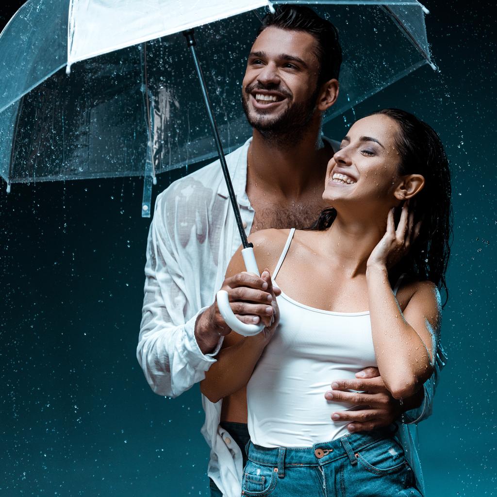 позитивний бородатий чоловік тримає парасольку і стоїть з веселою дівчиною на чорному
  - Фото, зображення