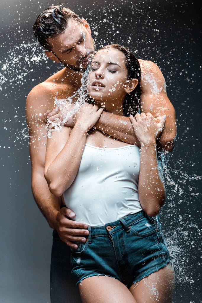 guapo y sin camisa hombre abrazando hermosa novia cerca de salpicadura de agua en negro
  - Foto, imagen
