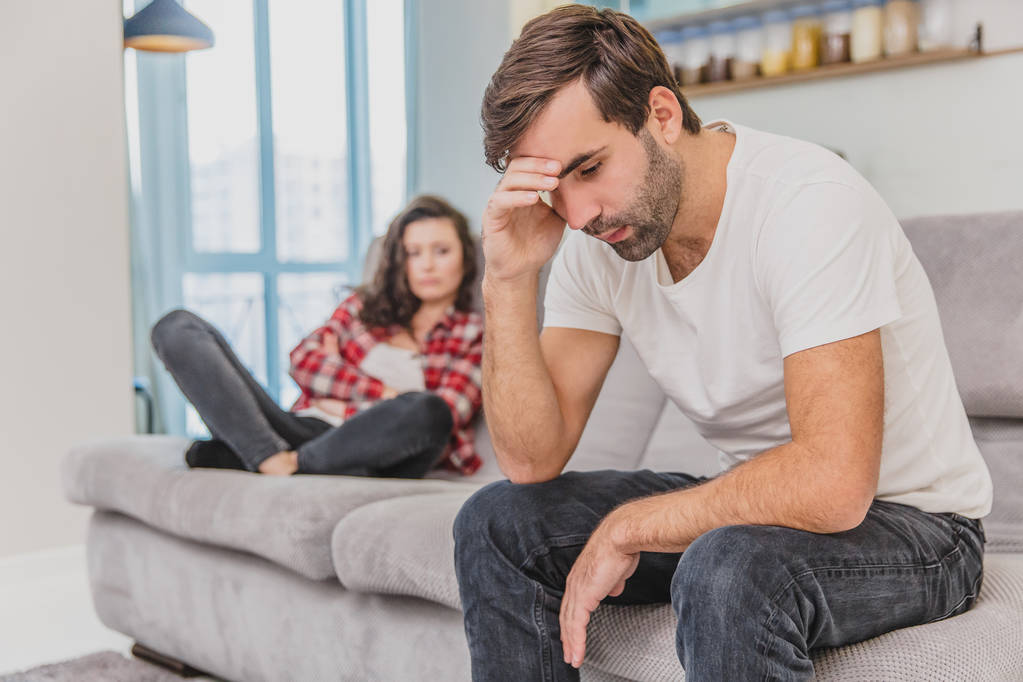 Couple argue. The wife shouted to her desperate husband, sitting on the couch in the living room at home. A man does not look at his wife. - Photo, Image