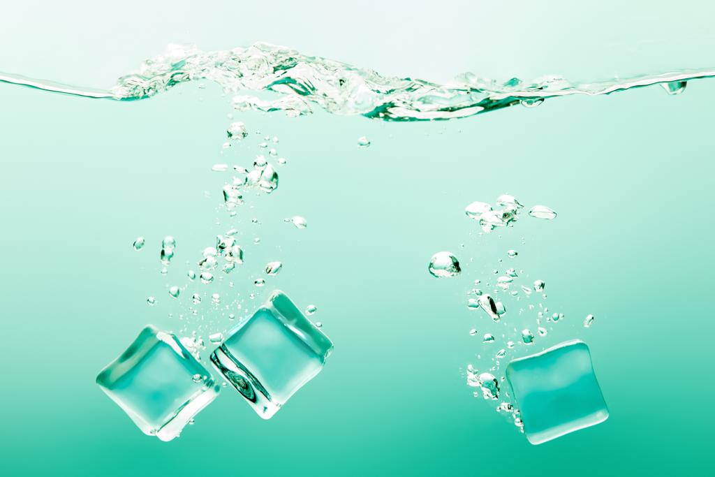 transparentes reines Wasser mit Blasen und Eiswürfeln auf grünem Hintergrund - Foto, Bild