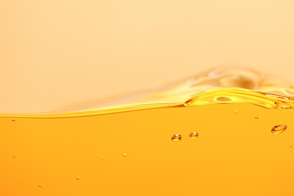 Vlnitá žlutá zářivá tekutina se šplouchnutím a bublinami izolovanými na žluté - Fotografie, Obrázek