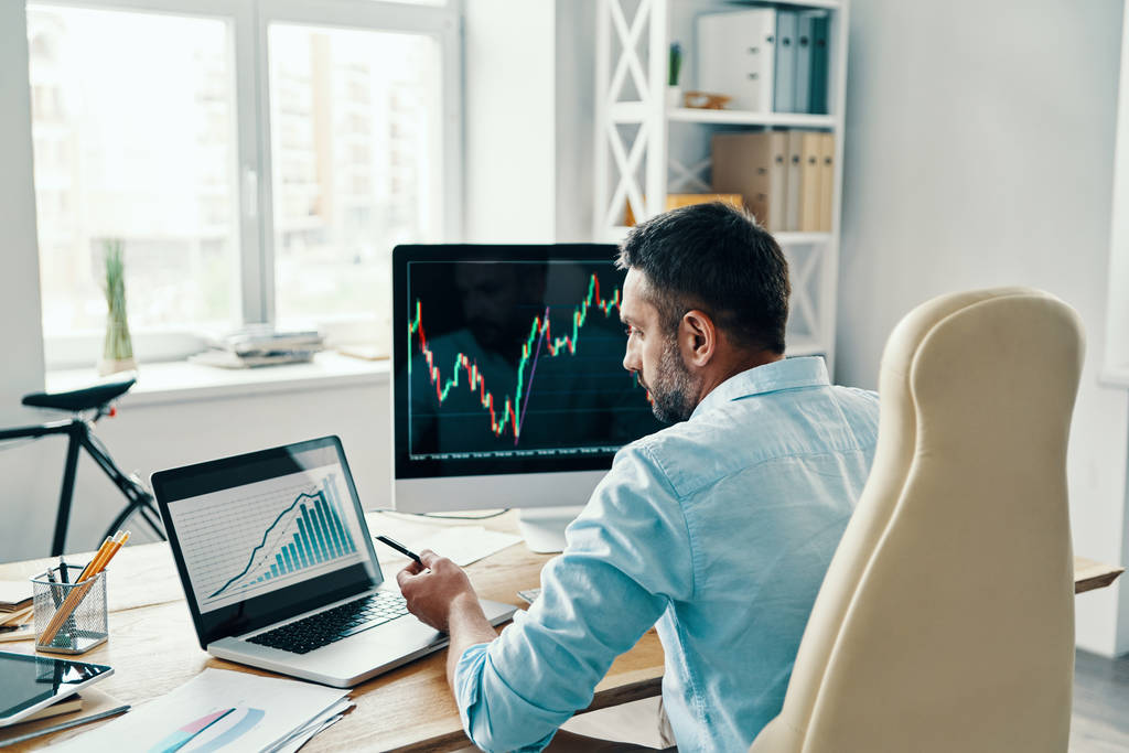 Zadní pohled na člověka v elegantní příležitostné práci analýza údajů o akciovém trhu při sezení v kanceláři   - Fotografie, Obrázek