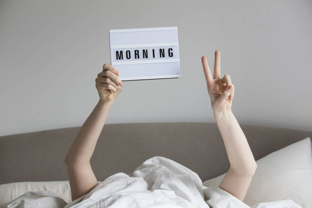 Vrouw in bed onder de lakens houden van een ochtend teken - Foto, afbeelding