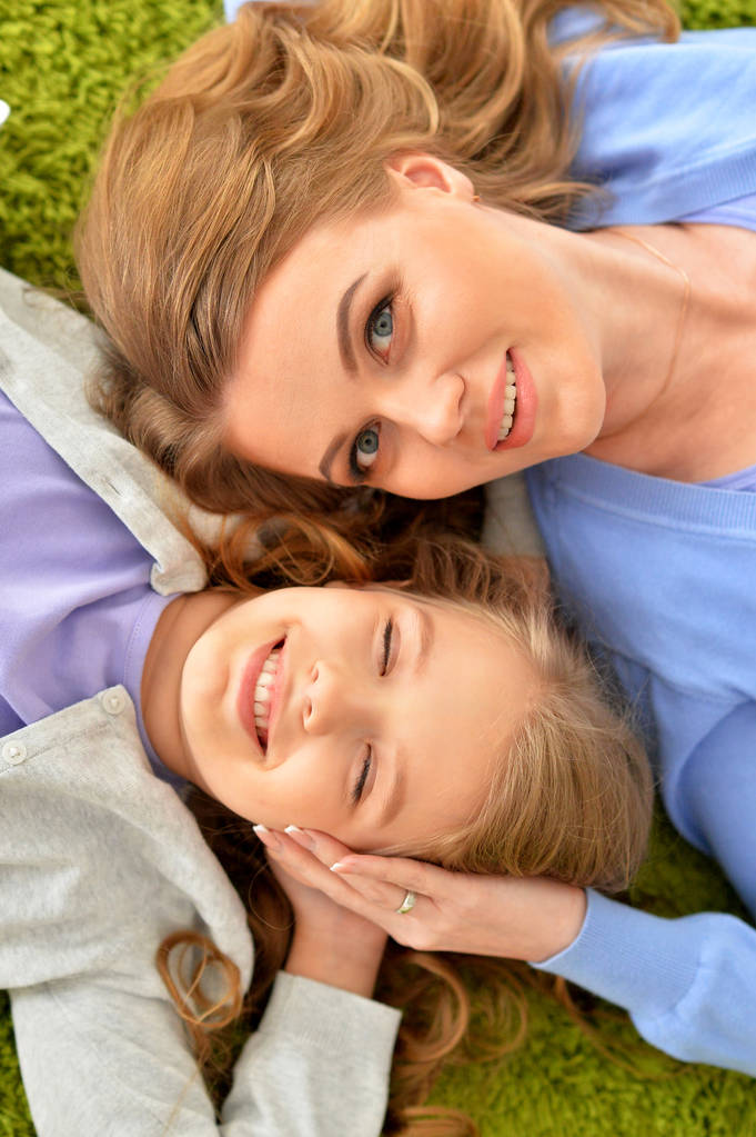 Mère heureuse avec sa fille allongée sur un tapis vert à la maison
 - Photo, image