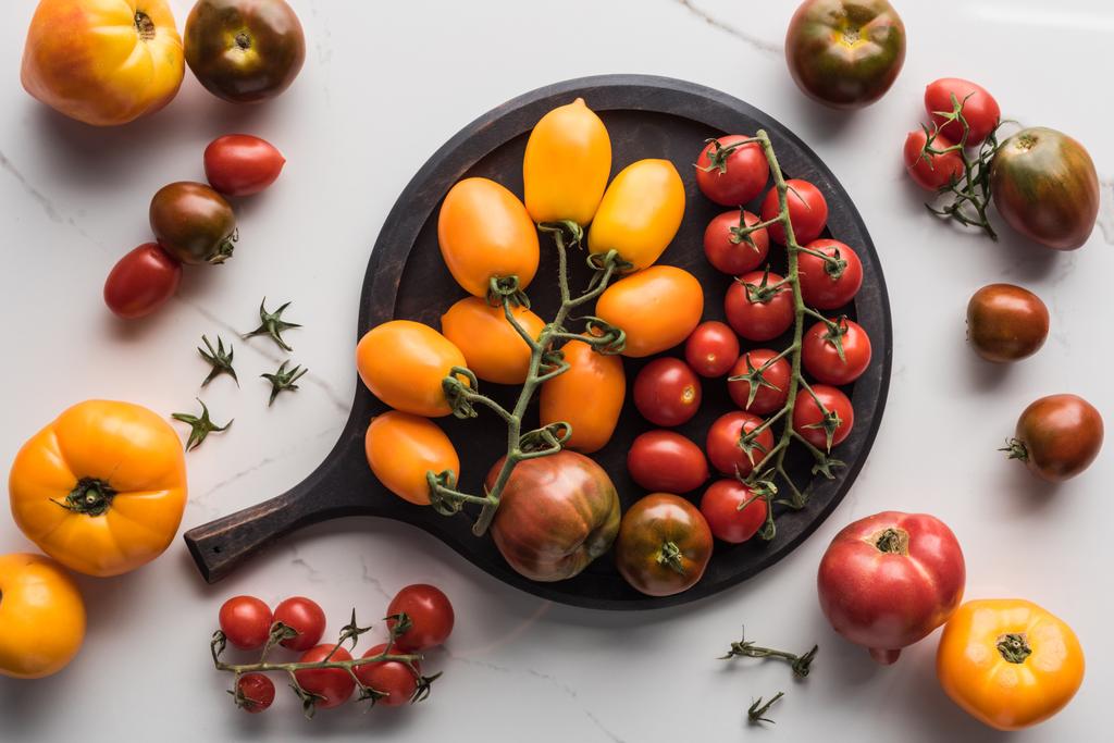 top view of different yellow, red and cherry tomatoes on pizza pan on marble surface  - Photo, Image