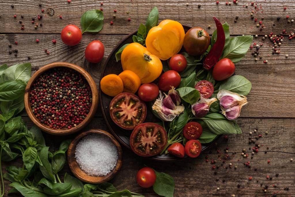 pohled na talíř se špenátem, česnekem a rajčaty nakrájenými v blízkosti pepře a misky na dřevěném stole  - Fotografie, Obrázek