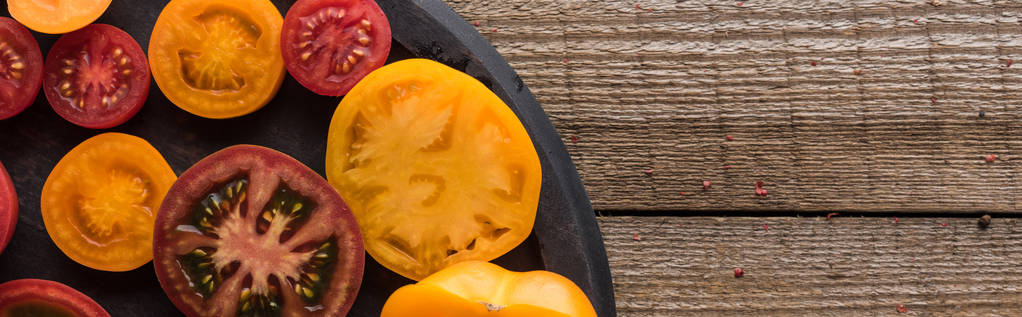 Panoramaaufnahme roter und gelber Tomaten auf Pizzapfanne auf Holztisch  - Foto, Bild