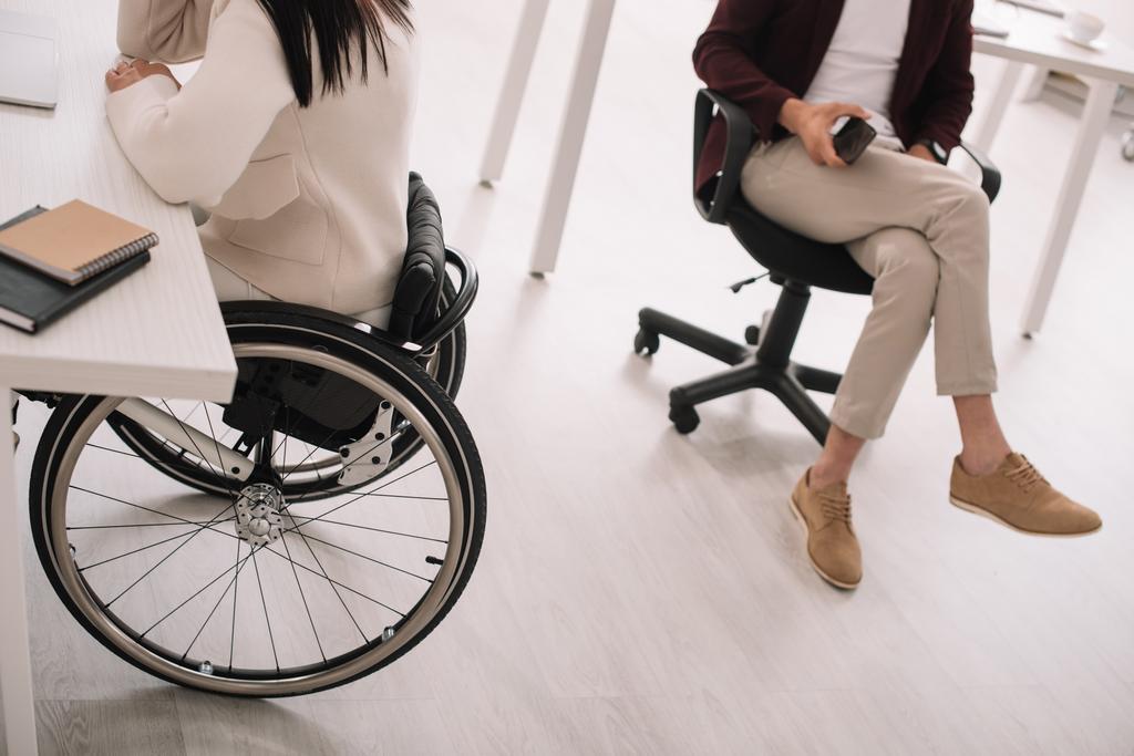 vista cortada de empresária em cadeira de rodas perto de parceiro de negócios no escritório
 - Foto, Imagem