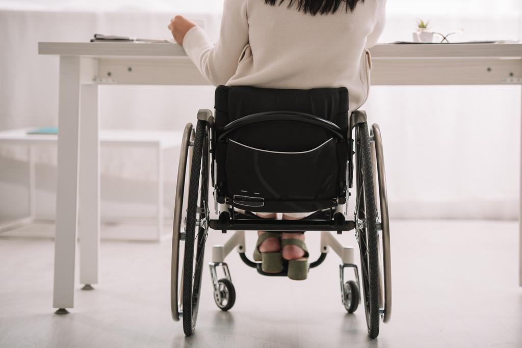 vista trasera de la mujer de negocios discapacitada sentada en silla de ruedas en el lugar de trabajo
 - Foto, Imagen