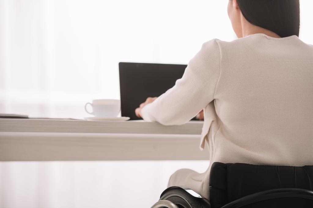 vista posterior de la mujer de negocios discapacitada usando el ordenador portátil mientras está sentado en el lugar de trabajo en la oficina
 - Foto, imagen