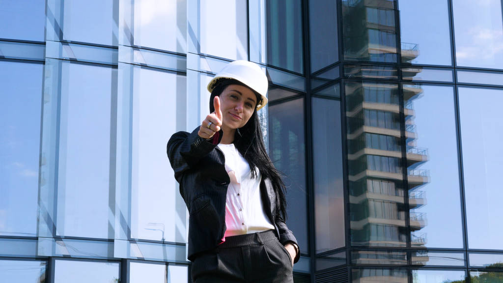 Business woman in suit and helment with crossed arms, looking at camera, smiling. Concept of: Skyscraper background, Communication, Manager, New business. - Photo, Image