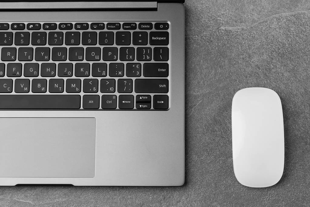 Werkplaats met open laptop met zwart scherm en muis op modern grijs stenen bureau, gefilterd beeld, focus op toetsenbord.Kantoortafel met notitieblok, computer. kopieer ruimte. horizontale foto - Foto, afbeelding