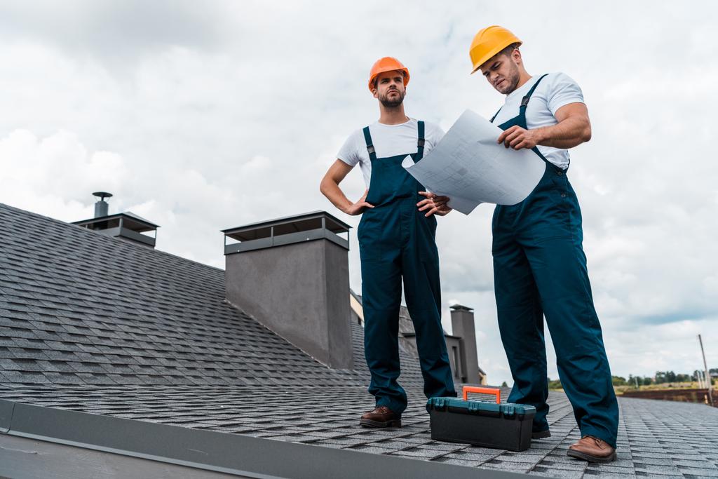 αρχιτέκτονας στέκεται στην οροφή με τα χέρια στους γοφούς κοντά συνάδελφο με χαρτί  - Φωτογραφία, εικόνα