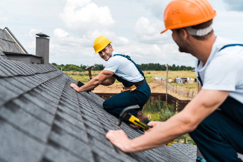 屋根の上の同僚を見て幸せな修理工の選択的な焦点  - 写真・画像