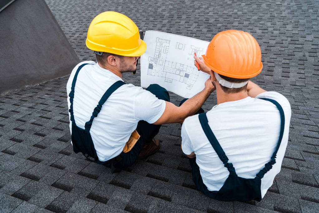 Blick von oben auf Bauarbeiter in Helmen, die den Bauplan betrachten  - Foto, Bild