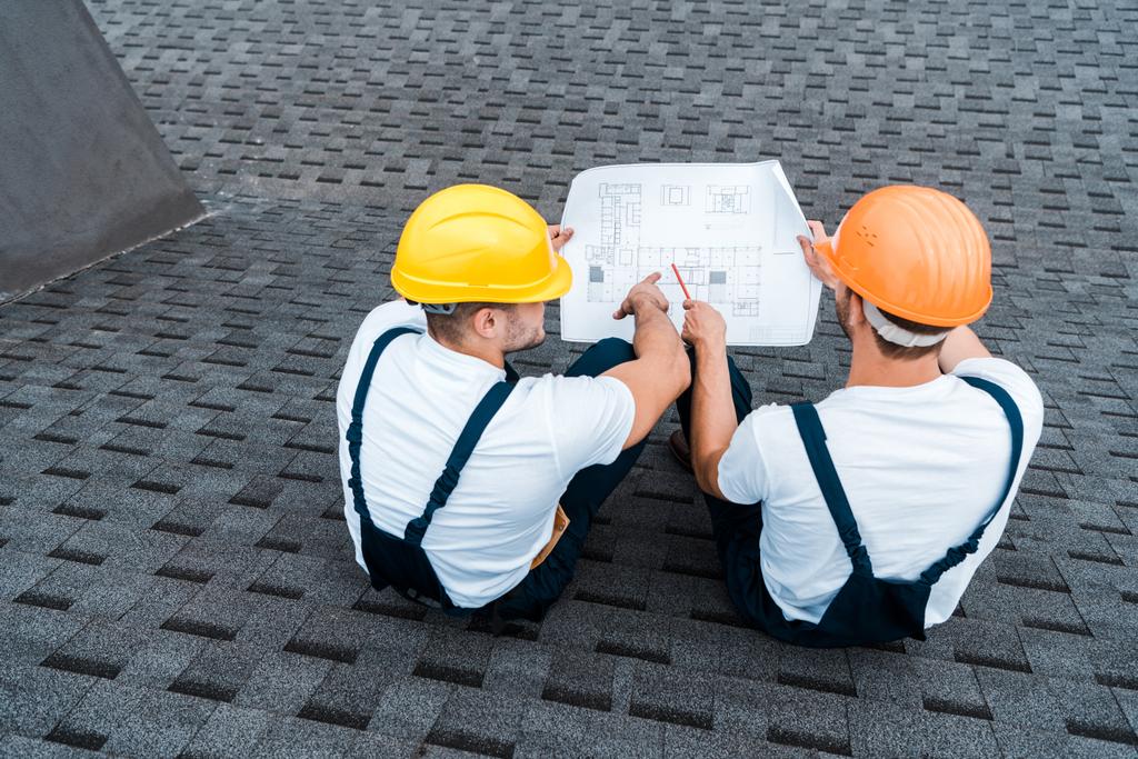 overhead view of architects in helmets sitting on roof with blueprint  - Photo, Image