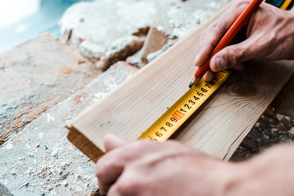 обрезанный вид мастера, держащего карандаш при измерении деревянной доски
  - Фото, изображение