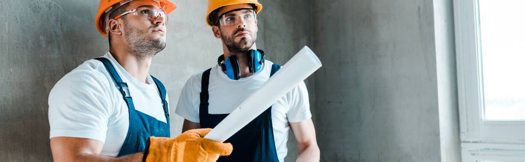 Panoramaaufnahme eines gutaussehenden Reparateurs, der Papierrolle in der Nähe eines Mitarbeiters hält  - Foto, Bild