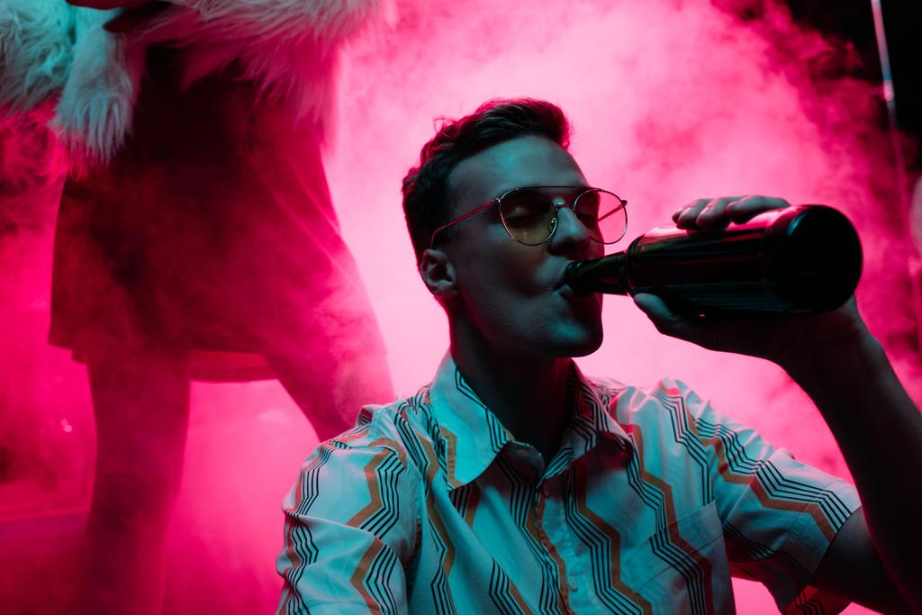handsome man in sunglasses drinking alcohol during rave in nightclub - Photo, Image