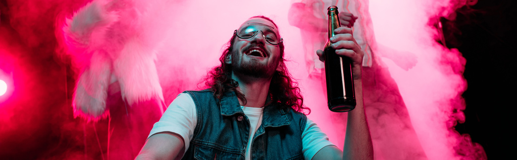 панорамний знімок людини в сонцезахисних окулярах з пляшкою алкоголю під час раю в нічному клубі
 - Фото, зображення