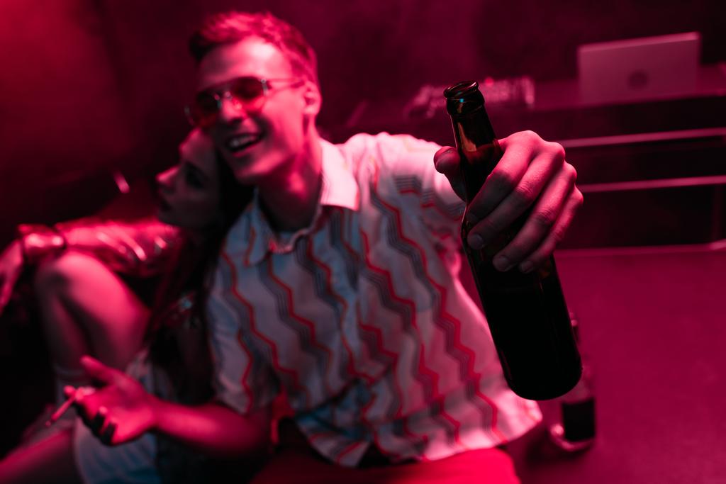 Lächelnder Mann mit Bier und Zigarette in der Nähe von Mädchen in Nachtclub bei Rave - Foto, Bild