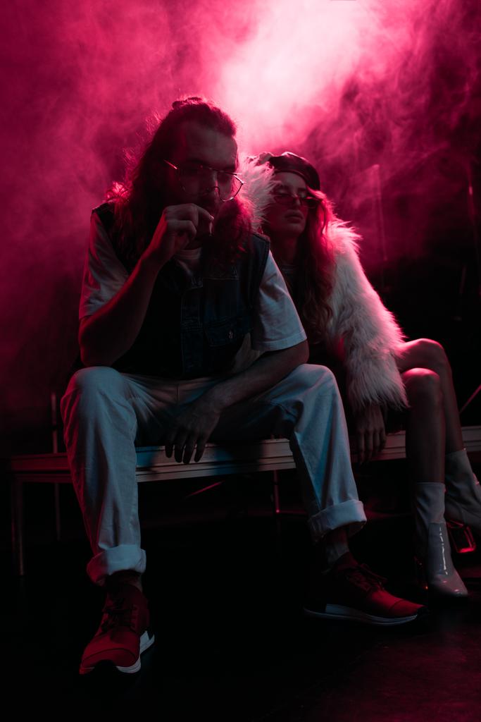 hombre fumando cigarrillo cerca de mujer joven durante fiesta rave en discoteca con humo rosa
 - Foto, Imagen