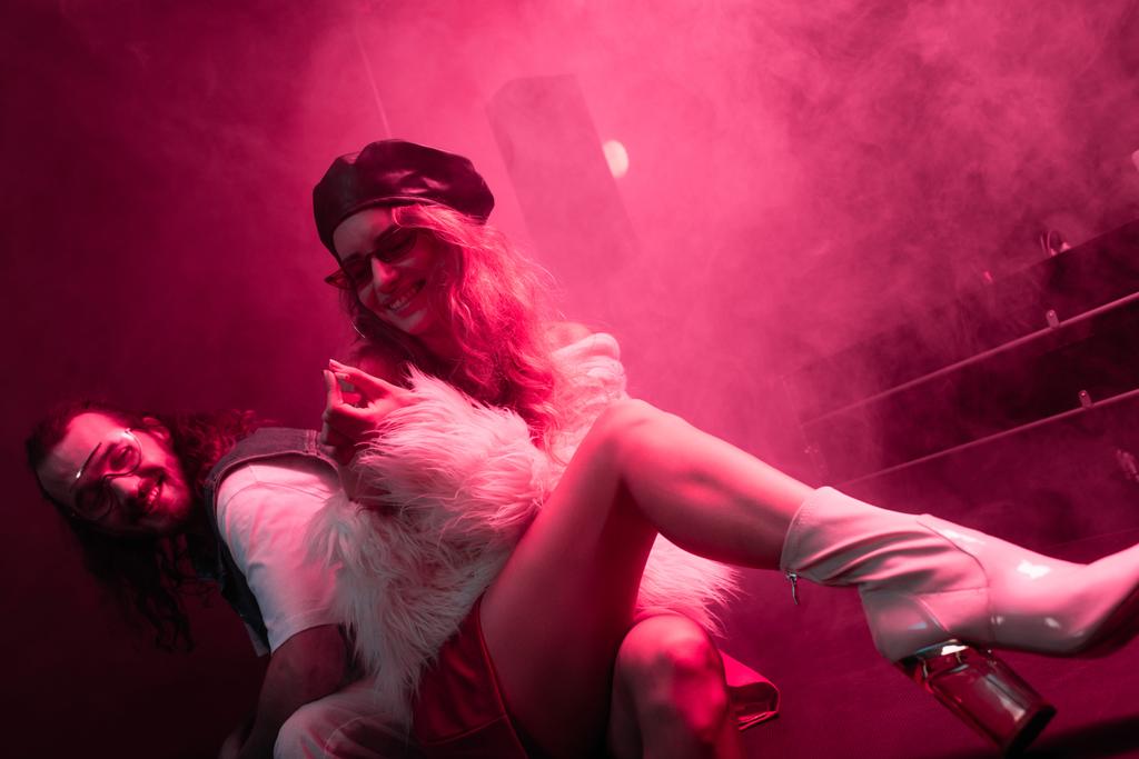 ナイトクラブでレイブパーティー中に男性の近くに座ってタバコを持つ若い女性 - 写真・画像