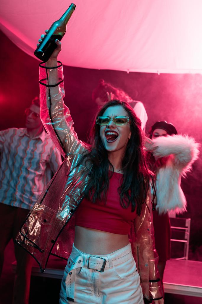 excited girl with bottle of alcohol during rave in nightclub - Photo, Image