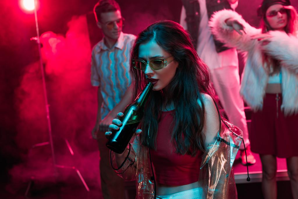 красивая девушка в солнечных очках пьет пиво в ночном клубе во время рейва
 - Фото, изображение