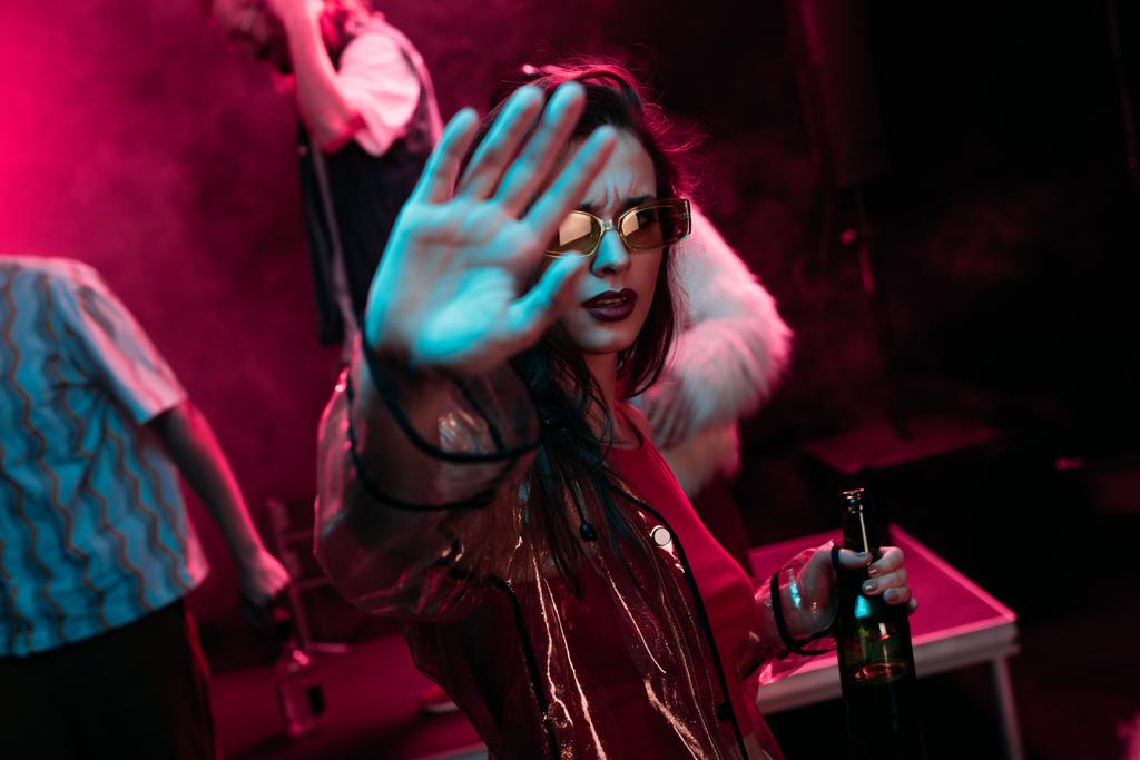 Девушка Жестикулирует руками и держит бутылку алкоголя во время рейва в ночном клубе
 - Фото, изображение
