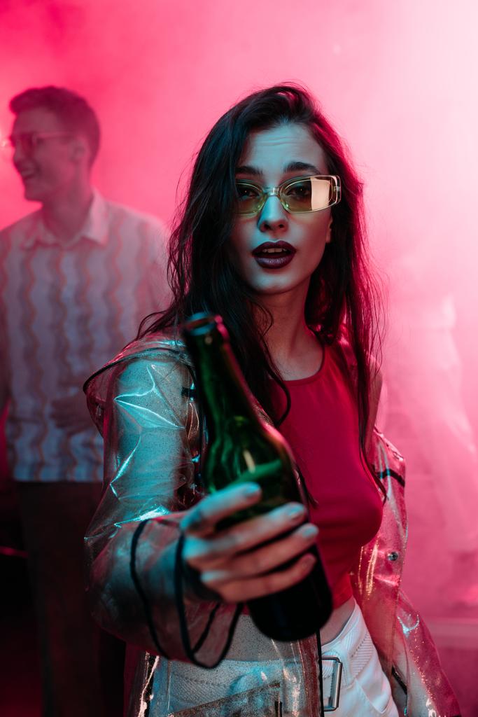κορίτσι σε γυαλιά ηλίου με μπουκάλι αλκοόλ κατά τη διάρκεια ρέιβ κλαμπ - Φωτογραφία, εικόνα