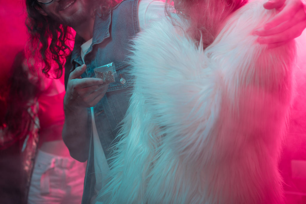 abgeschnittene Ansicht eines Mannes, der einem Mädchen in einem Nachtclub Unkraut in einer Plastiktüte mit Reißverschluss verabreicht - Foto, Bild