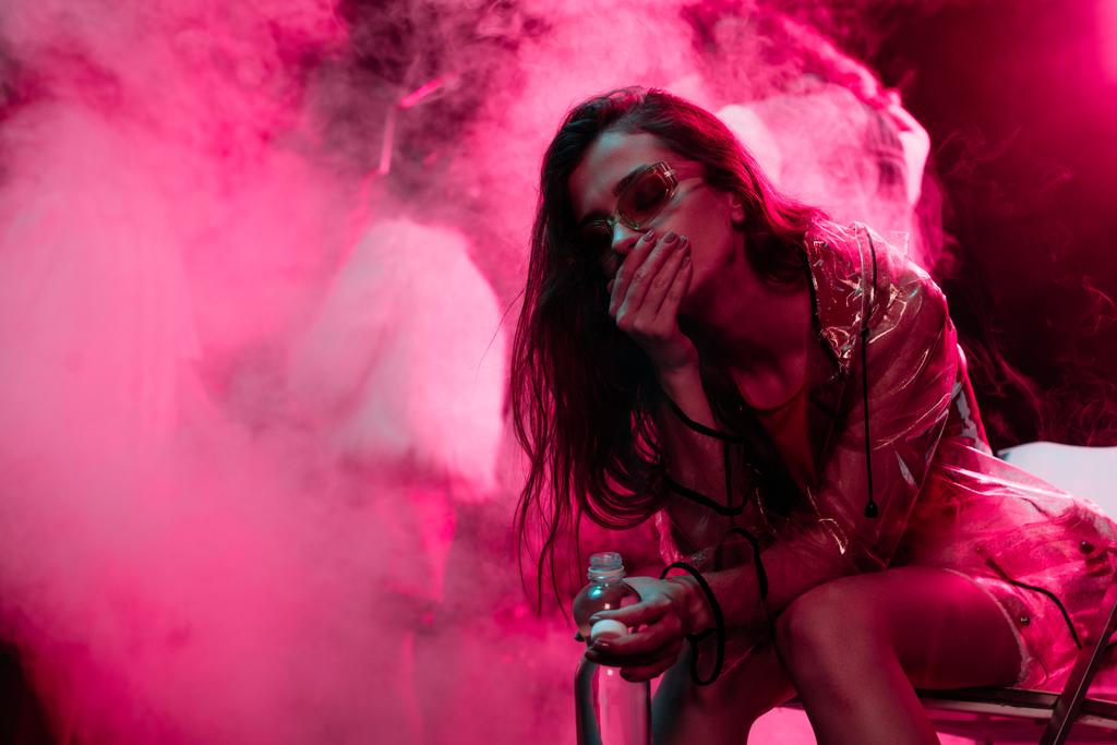 Krankes Mädchen sitzt mit Wasserflasche in Nachtclub - Foto, Bild