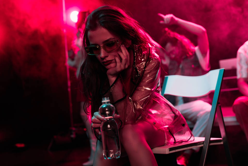больная молодая женщина сидит с бутылкой воды в ночном клубе
 - Фото, изображение