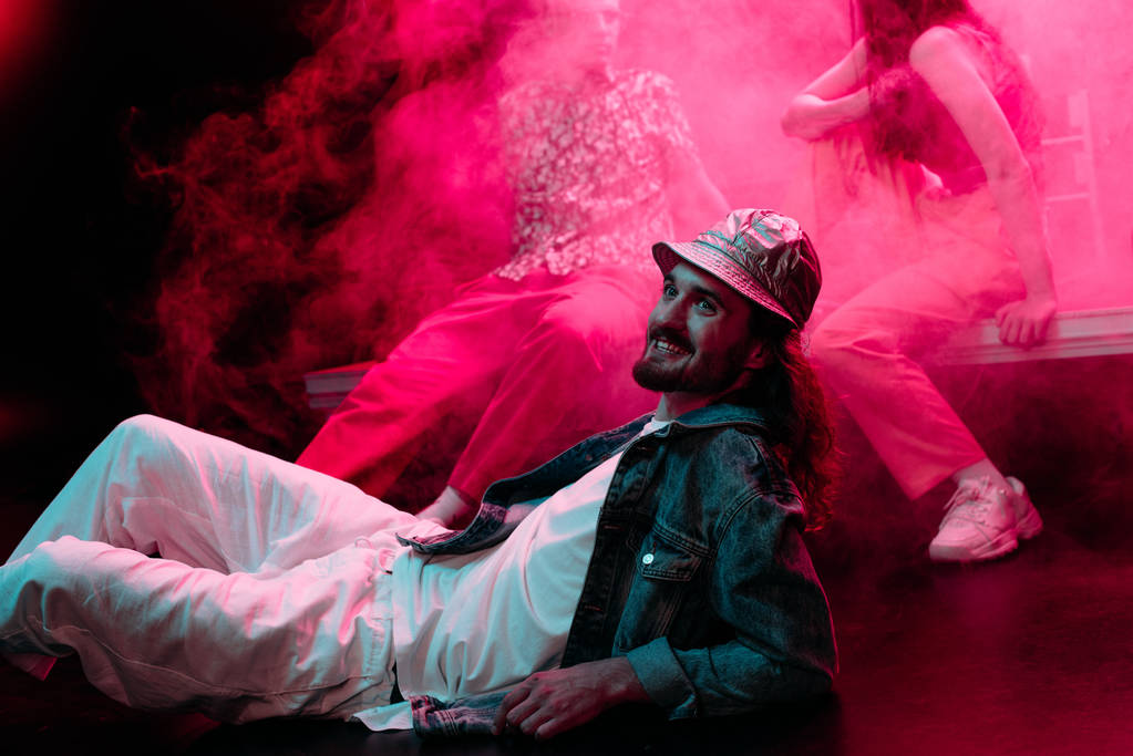 ピンクの煙でレイブパーティー中にナイトクラブで床に横たわっている笑顔の男 - 写真・画像