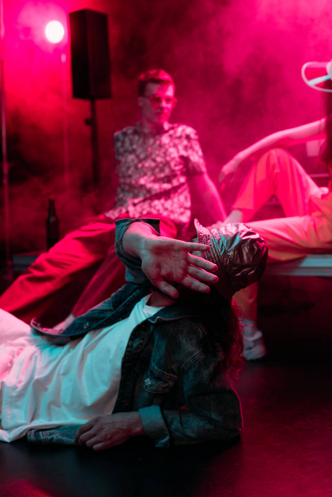 selectieve focus van de mens liggend op de vloer in nachtclub en bedekt gezicht - Foto, afbeelding