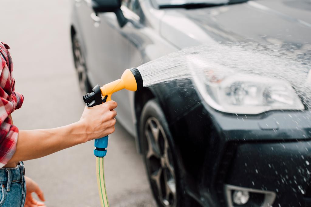 oříznutý pohled ženy mytí černého auta při přidržením tlakové podložky  - Fotografie, Obrázek